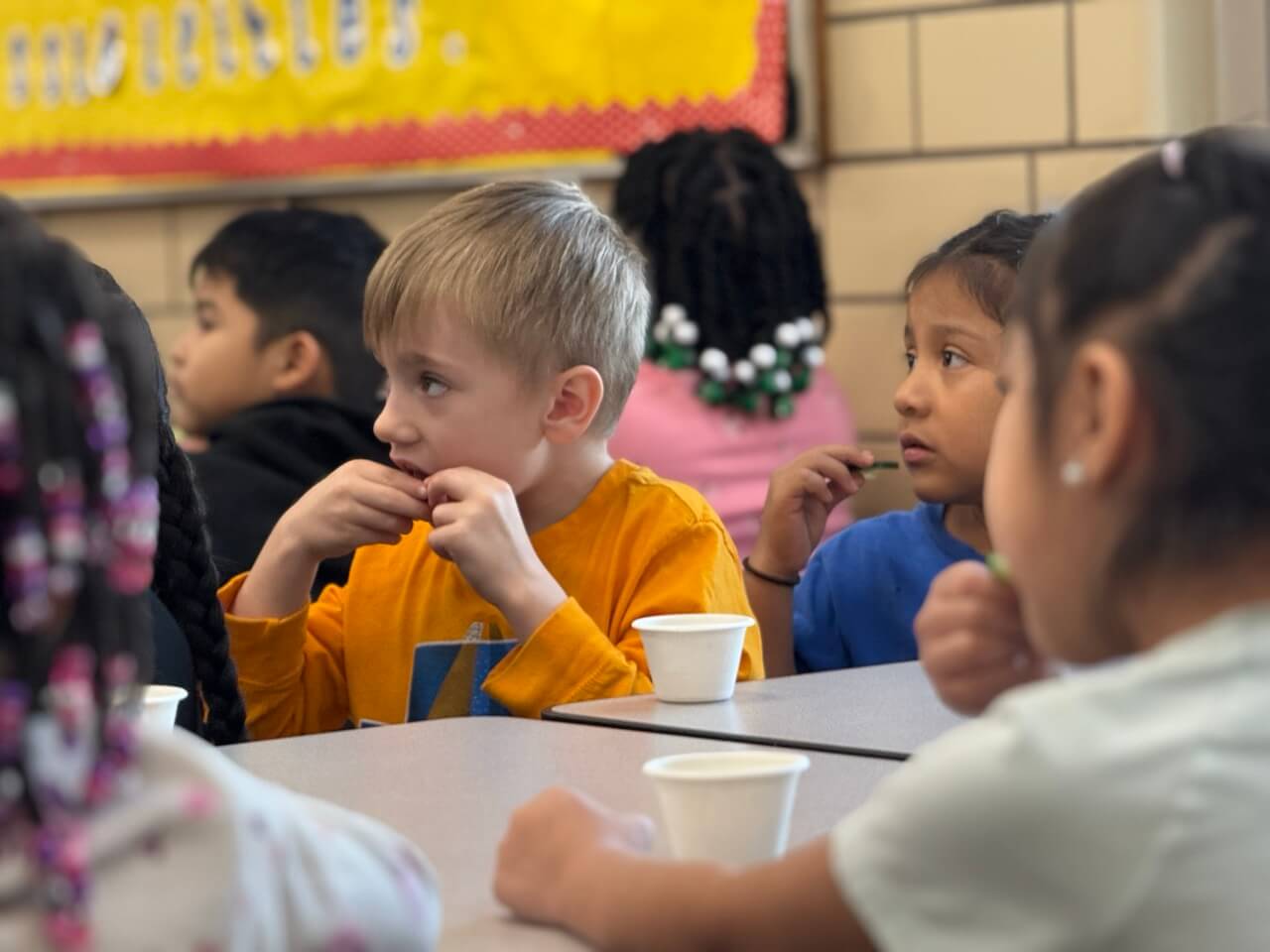 Young children sitting at school lunch table eating a sample of cucumbers from their produce taste testing cups