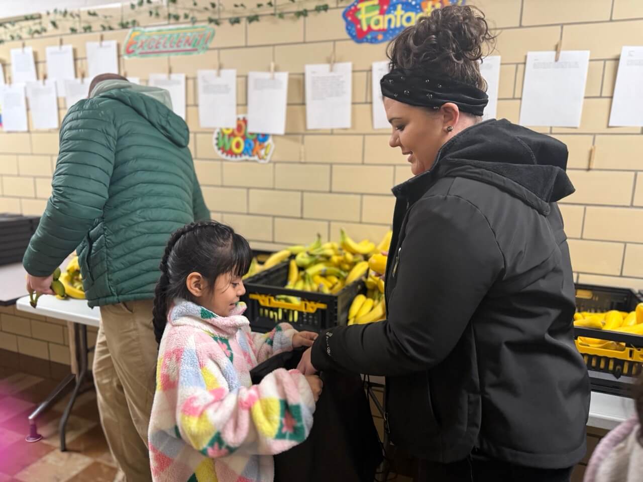 A woman volunteer from Lowe's placing a yellow squash in a young girl's Burrow Bag 